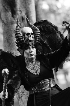 Woman in a gothic costume with skull headdress and wings in a forest.
