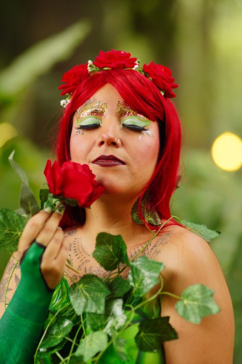 Free A woman in vibrant costume, surrounded by greenery, holding a red rose. Stock Photo