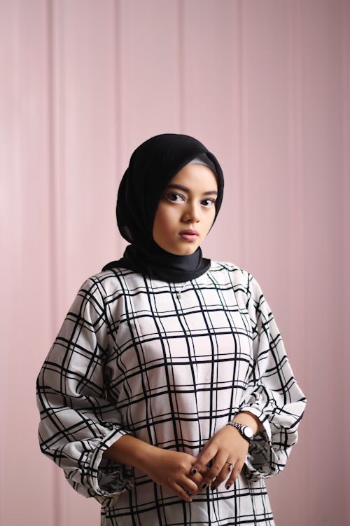 Wanita Mengenakan Gaun Bermotif Kotak Putih Hitam Dan Hijab Hitam Berdiri Dekat Dinding