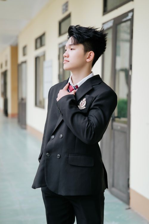 Free A student wearing a formal school uniform standing confidently in a hallway with natural lighting. Stock Photo