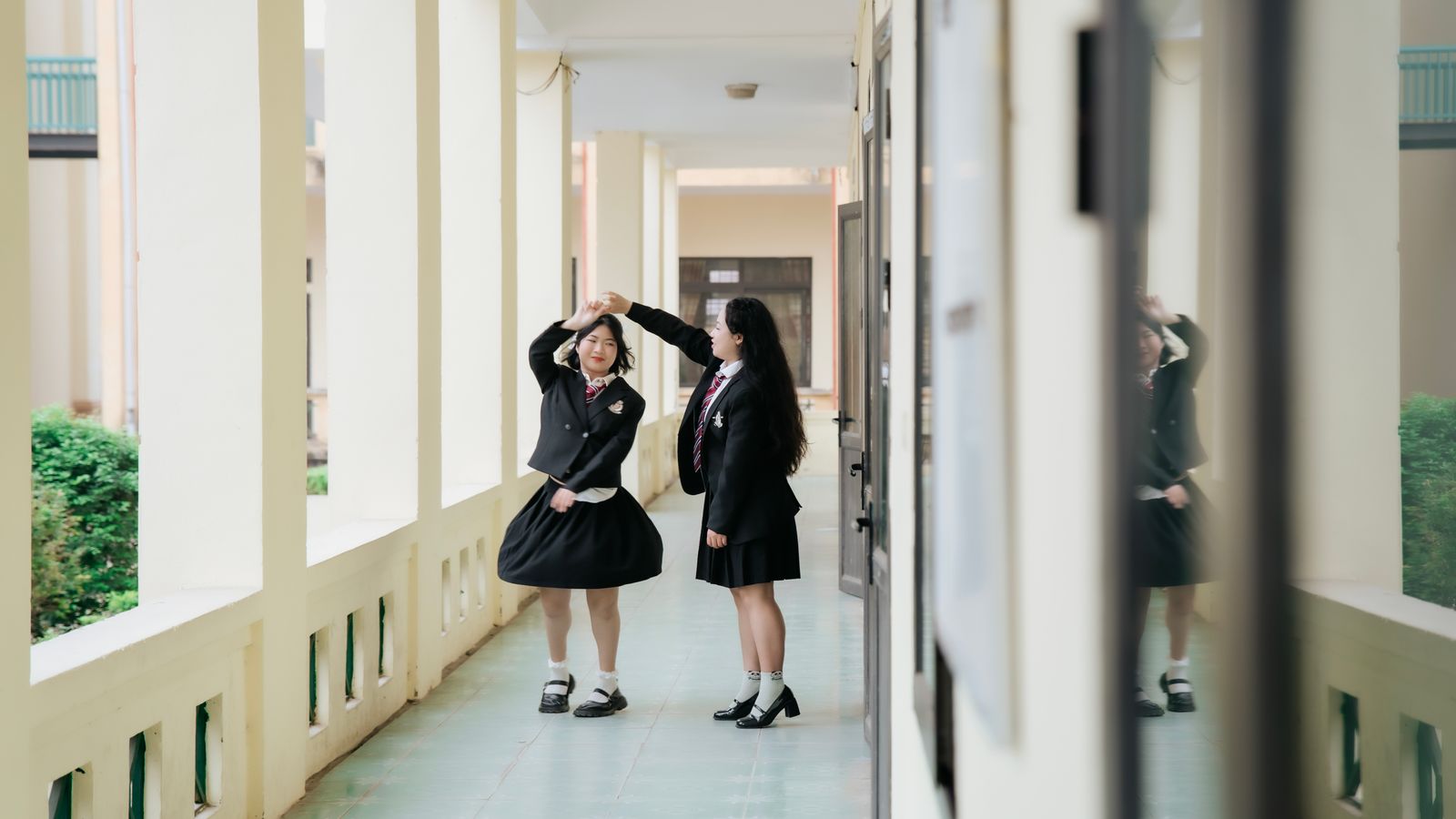 Two teenage students in uniform standing in a school corridor, engaging in conversation.