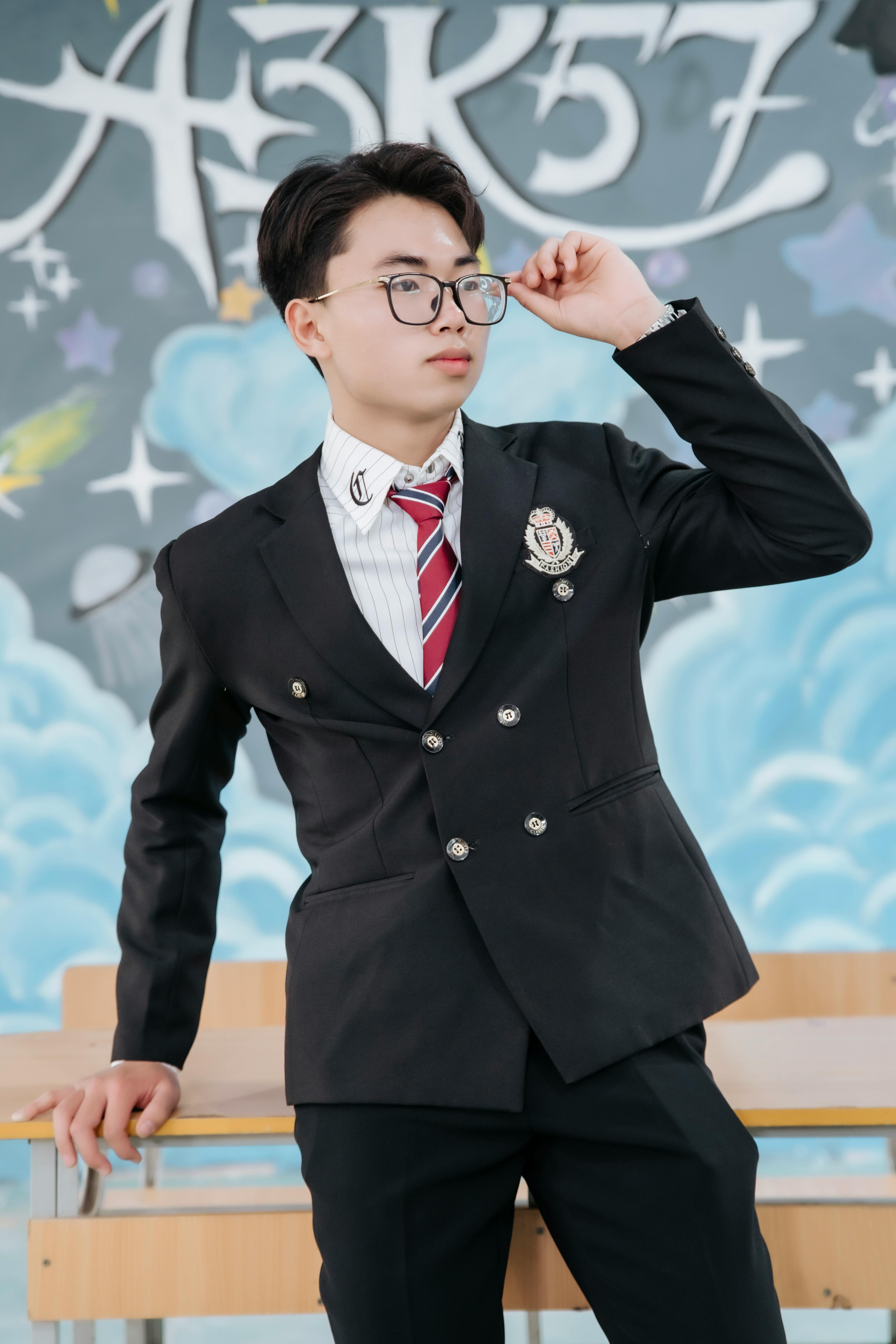 Confident young adult in a formal suit adjusting glasses in a colorful setting, exuding professionalism and style.