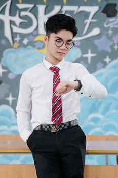 Young man in smart attire checking time against artistic graffiti background.