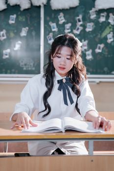 Young woman in uniform focused on reading at school desk with a decorated chalkboard background.