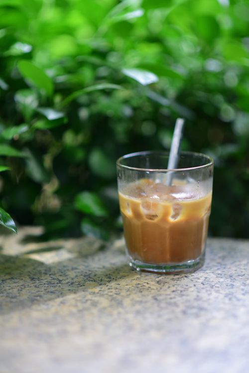 Free Refreshing iced coffee in a glass with straw on a table against green leafy backdrop. Stock Photo