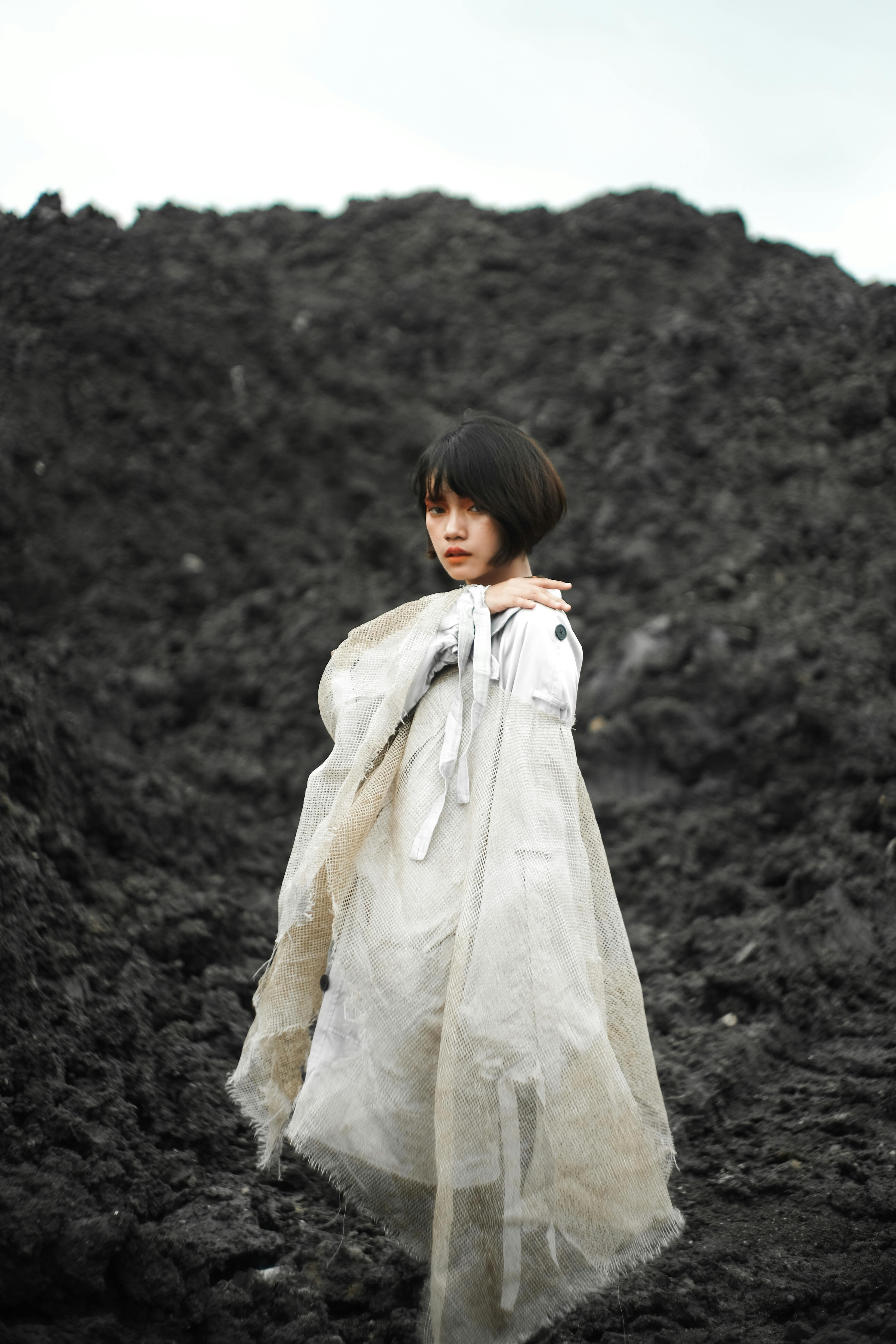 一名妇女站在贫瘠的岩石背景下，裹着白色织物