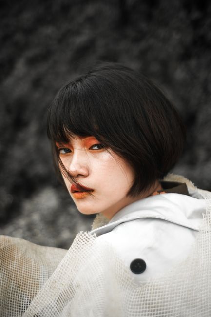 Close-up artistic portrait of a young woman with dramatic makeup and a textured outfit.