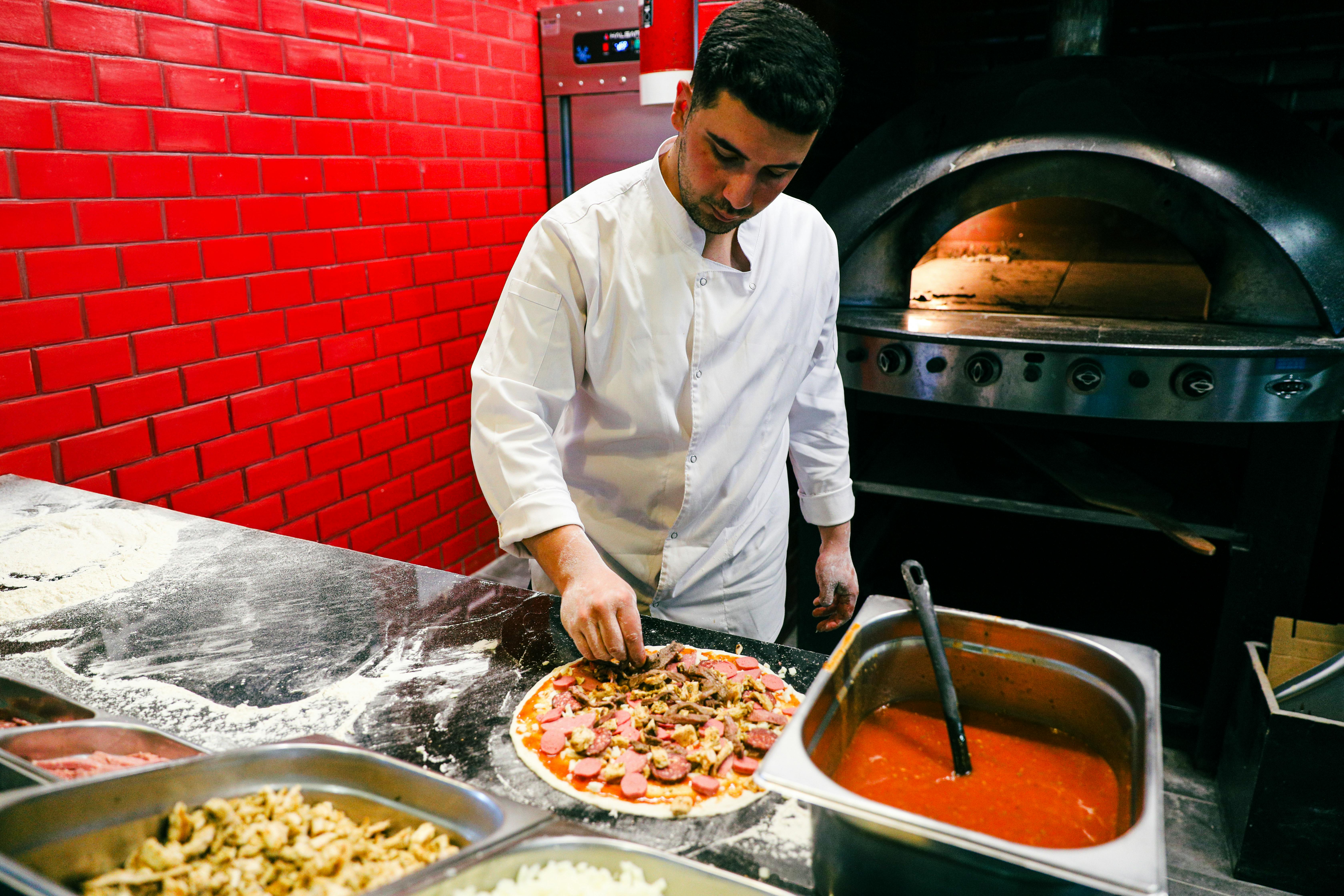 Chef in white uniform preparing pizza in a brick oven kitchen.