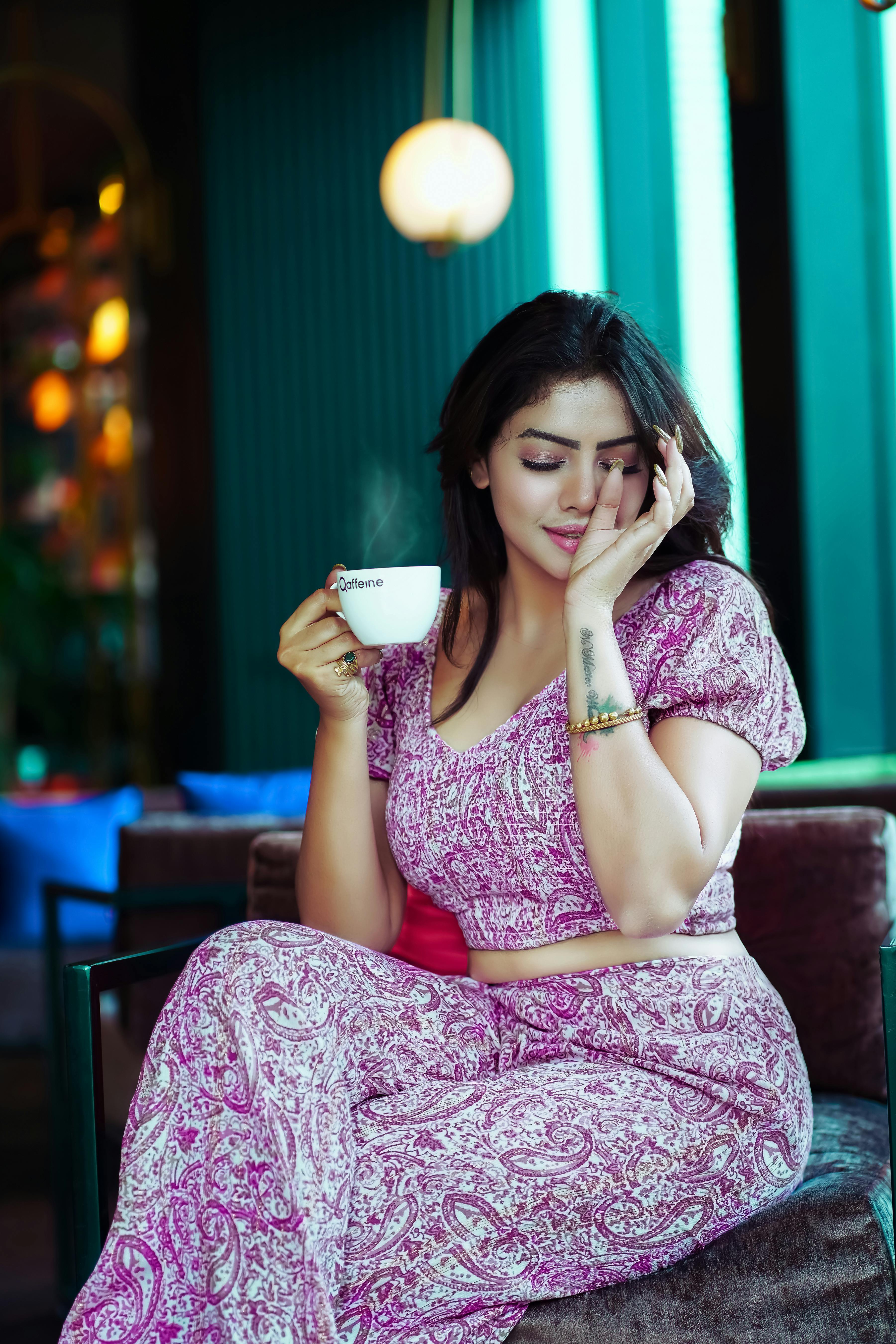 Free Beautiful woman in a stylish dress enjoying coffee indoors with a serene expression. Stock Photo