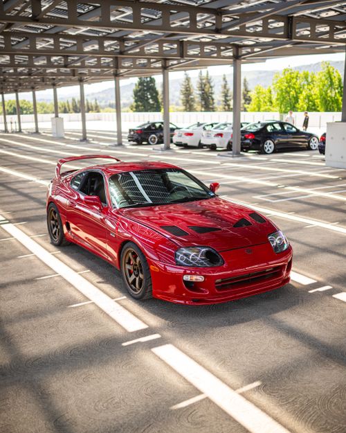 Free Red sports car parked in an industrial, sunlit parking space Stock Photo