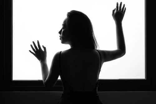 Free Black and white silhouette of a woman posing against a window, creating a dramatic scene. Stock Photo
