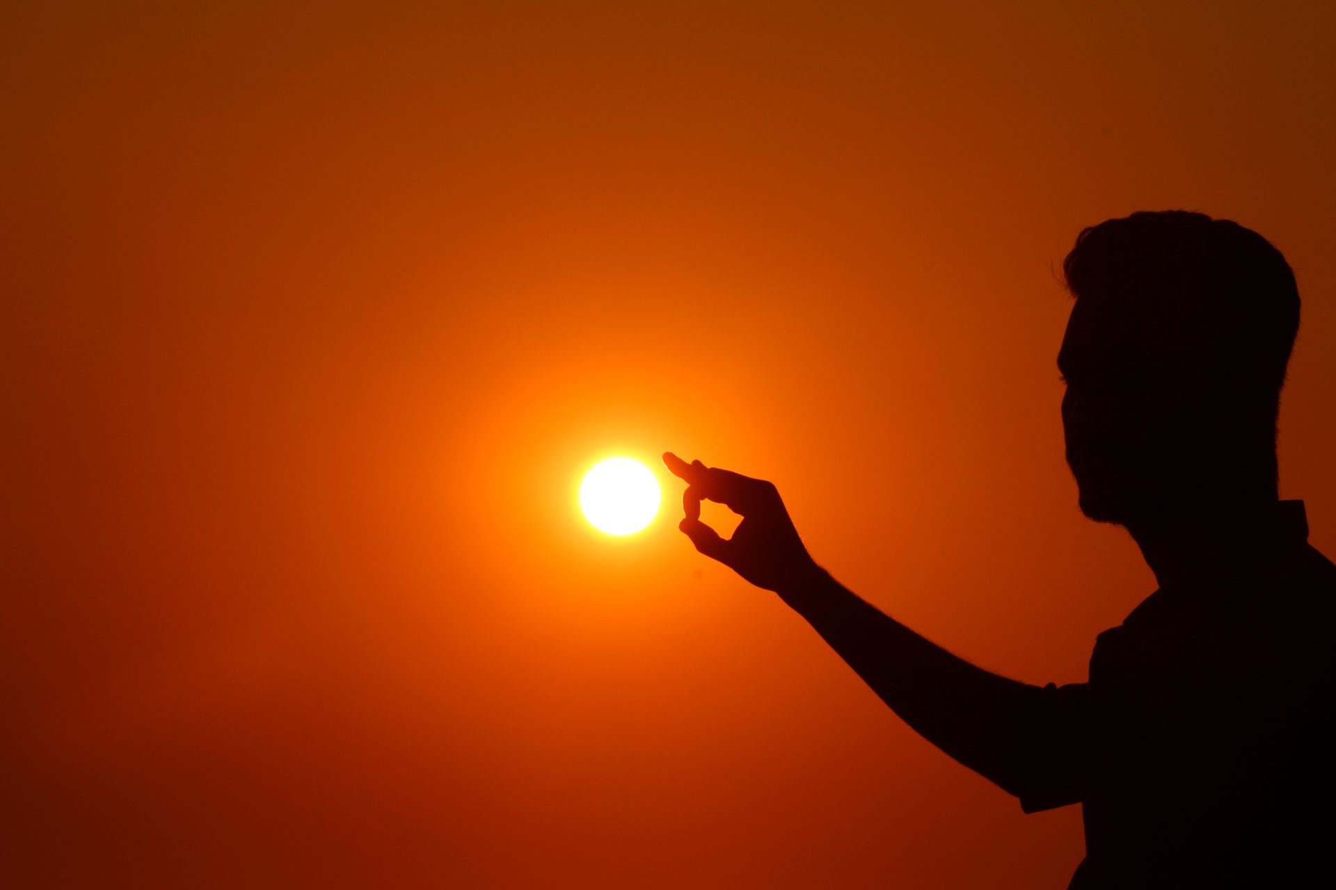 Captivating silhouette of a man appearing to hold the sun with a dramatic sunset backdrop.