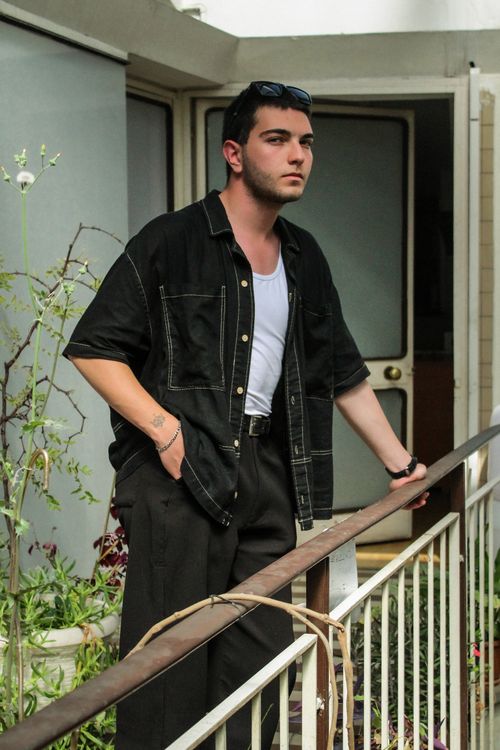 Free Young man in casual attire leaning on a railing, enjoying a moment outdoors. Stock Photo