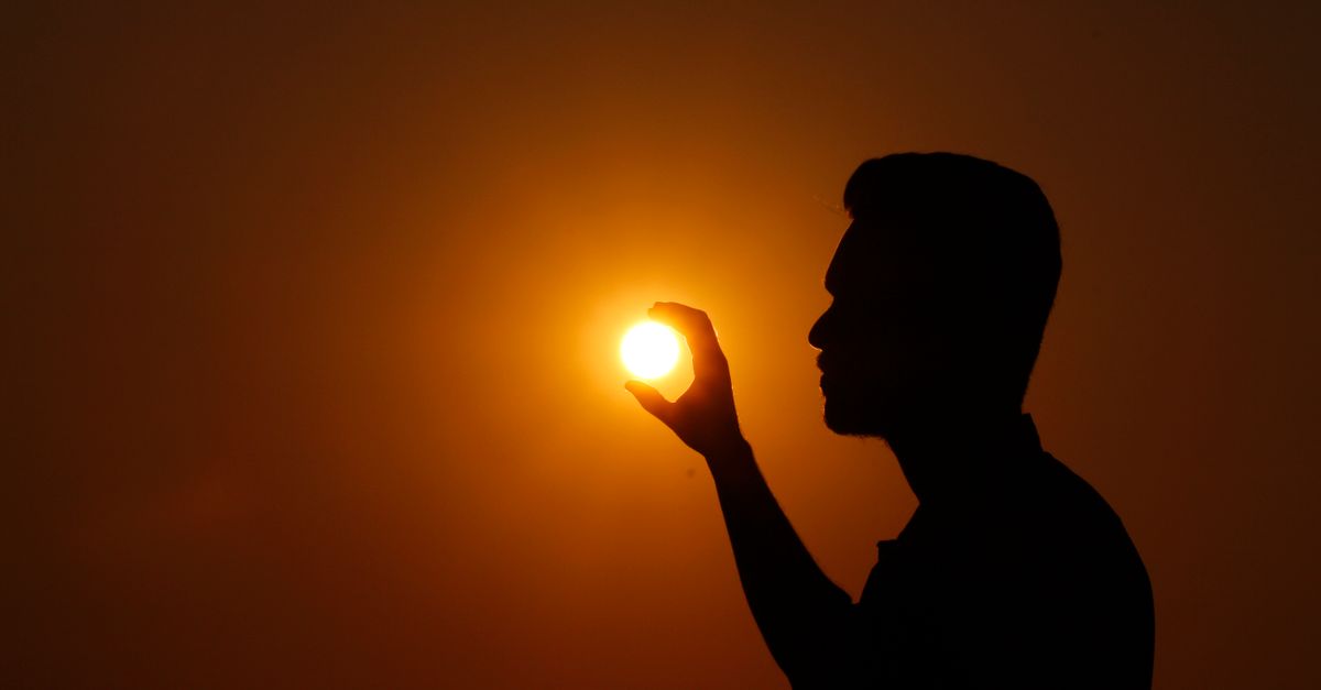 Artistic silhouette of a man seeming to hold the sun during a dramatic sunset.