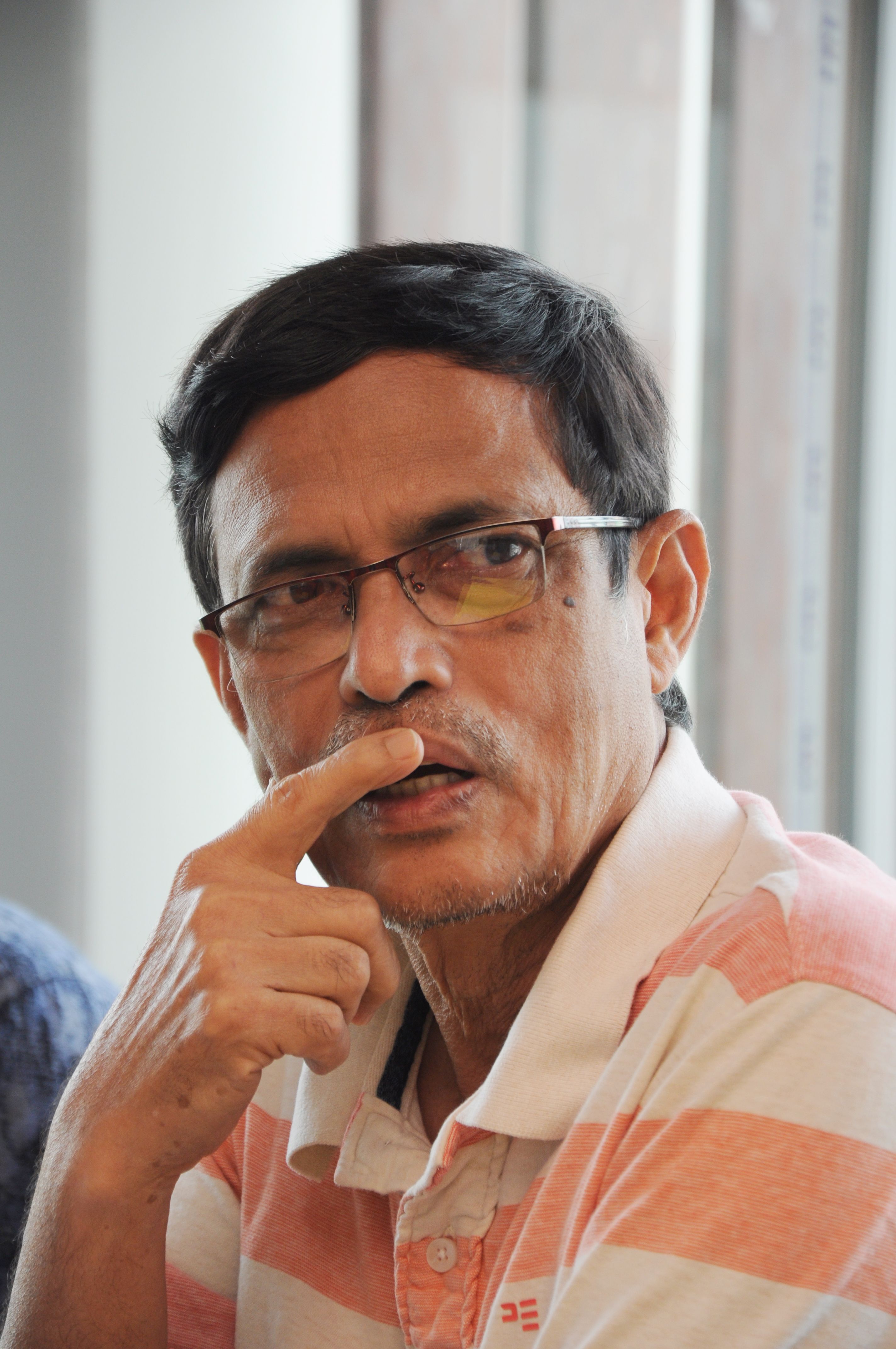 Middle-aged man wearing glasses, thoughtful expression, striped shirt, indoors.
