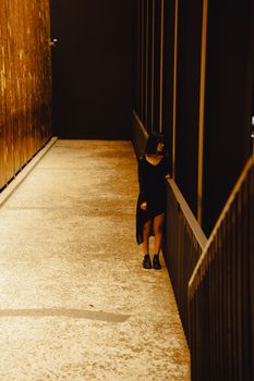 A woman in a stylish dress stands in a dimly lit urban alleyway, exuding a moody and mysterious vibe.
