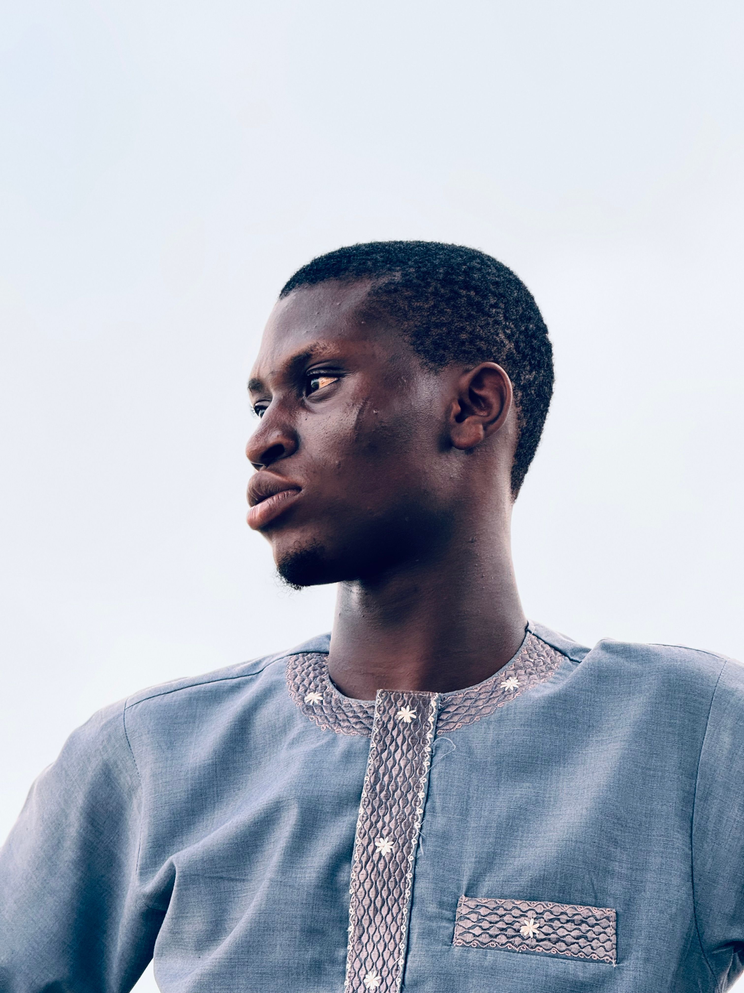 A man gazes thoughtfully, wearing traditional Nigerian clothing against a clear sky backdrop.