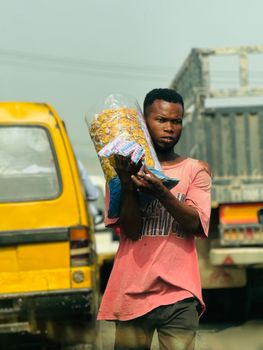 Young male street vendor holding snacks amidst busy urban traffic.