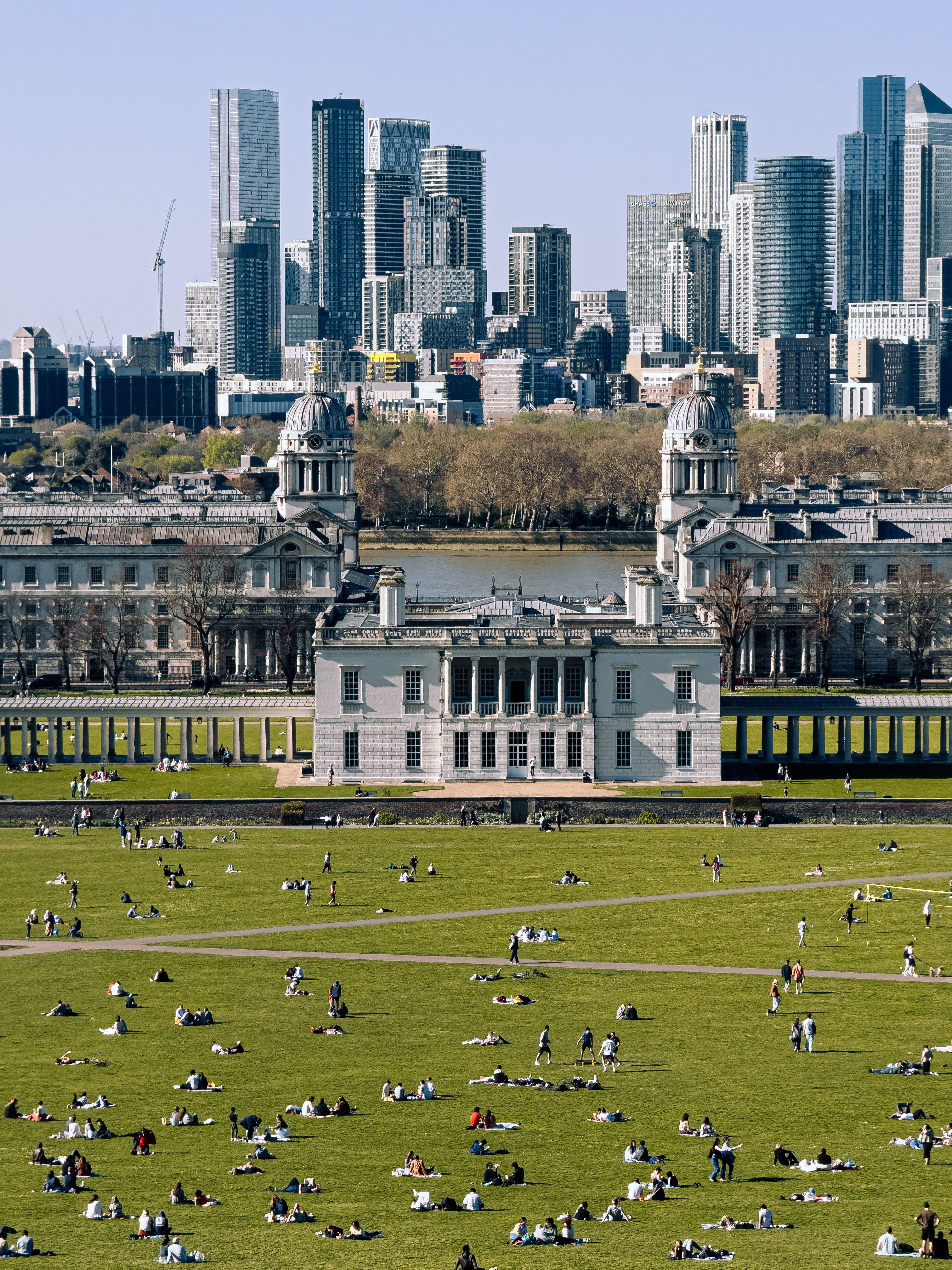 A vibrant scene of people enjoying Greenwich Park with London's skyline in the background.