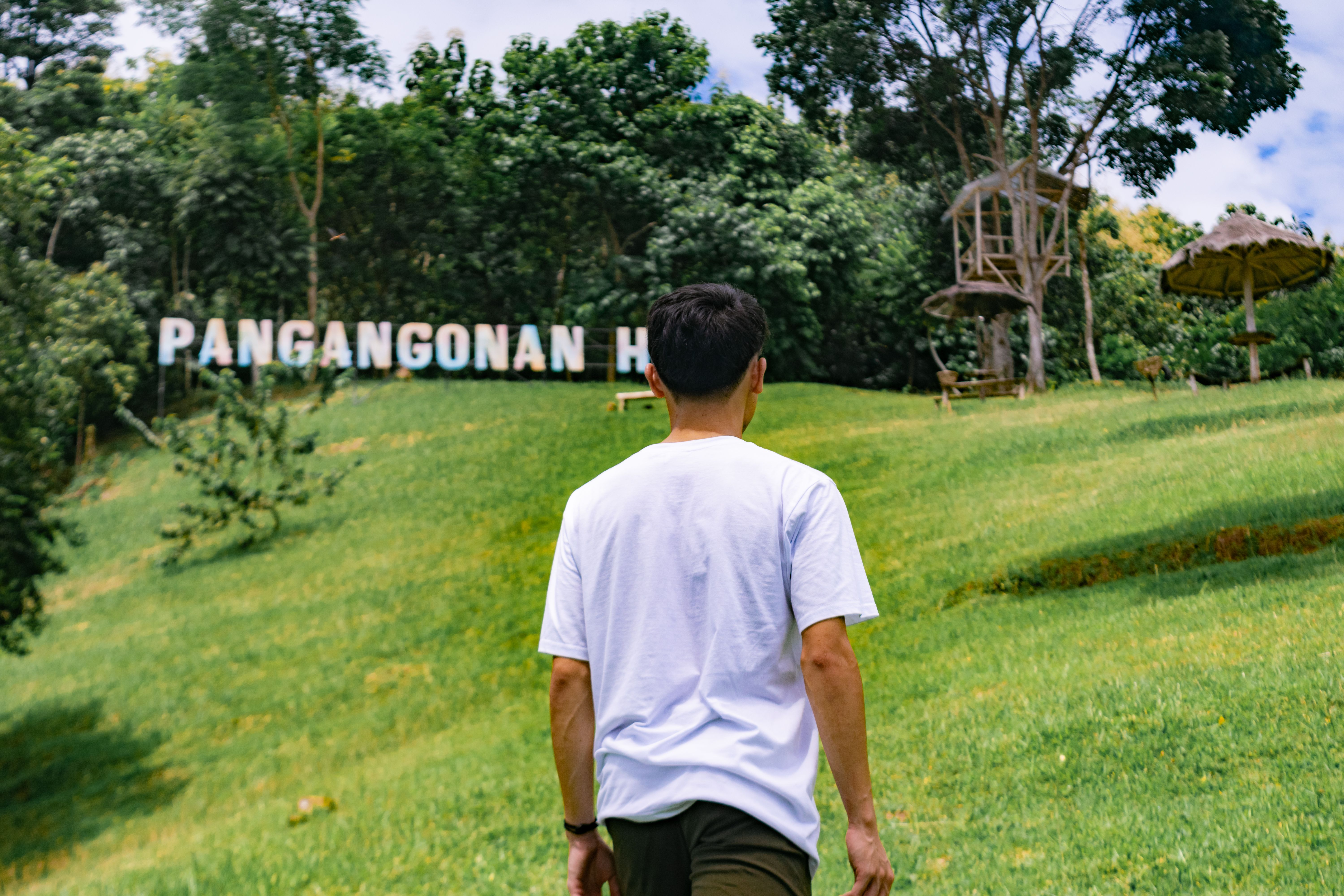 A person walking towards Pangangonan Hill, surrounded by lush greenery and a bright sky. - Fotografer Sidoarjo