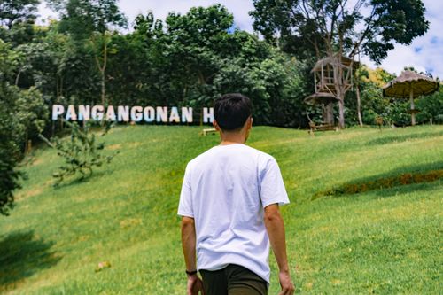 Free A person walking towards Pangangonan Hill, surrounded by lush greenery and a bright sky. Stock Photo