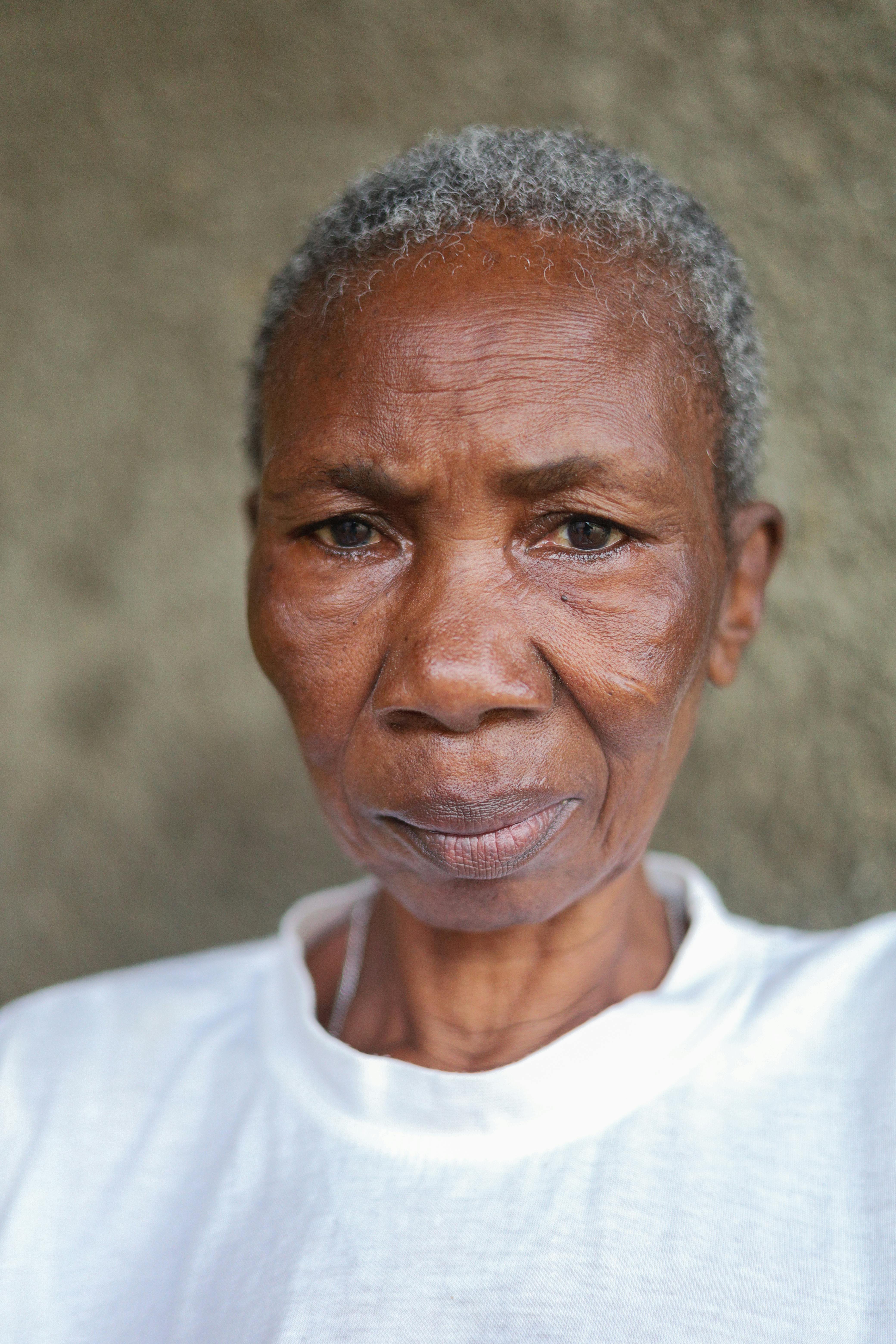 Close-up portrait of a senior woman with gray hair and pensive expression outdoors.