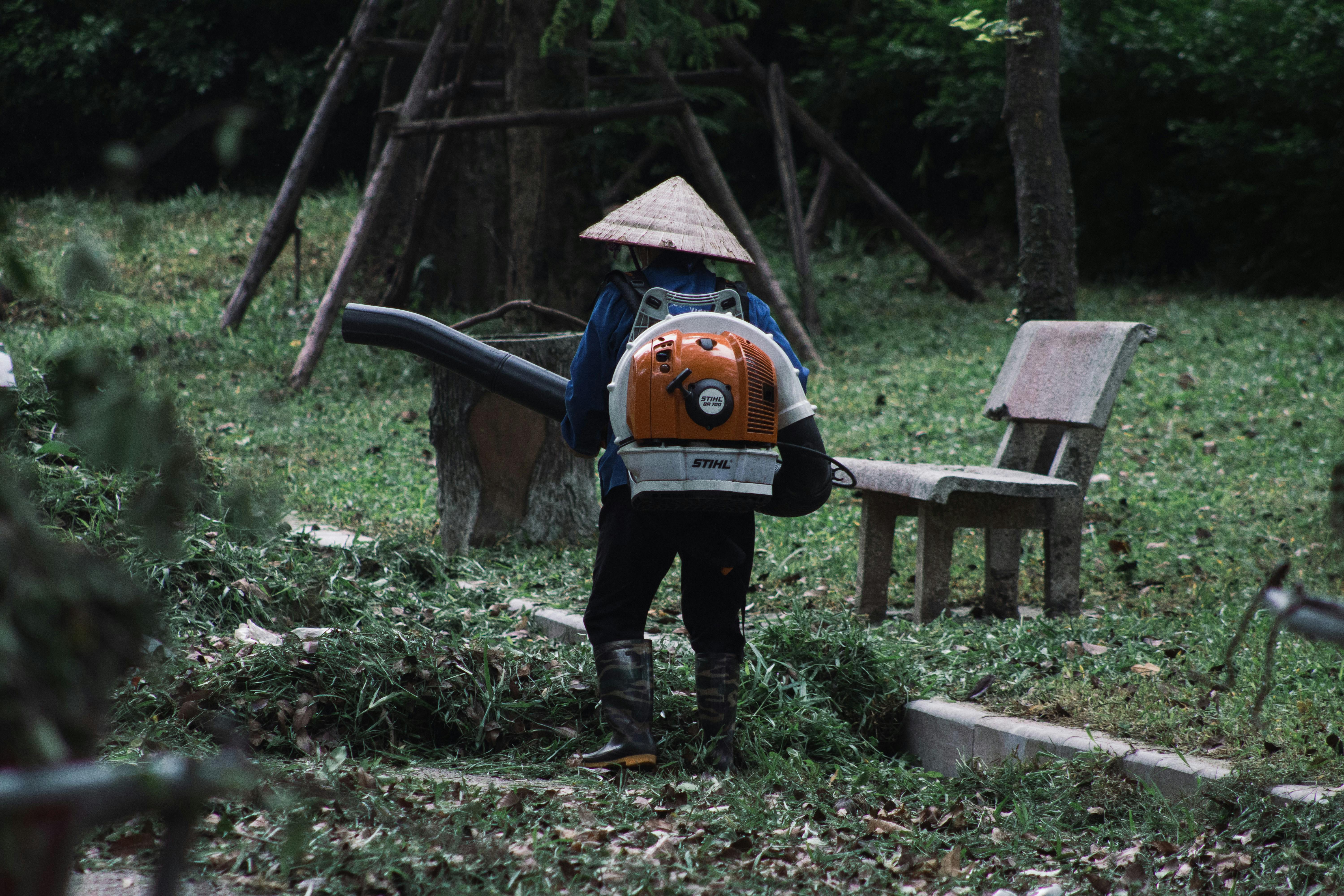 A gardener with a leaf blower maintains a park in Hanoi, Vietnam, surrounded by greenery.