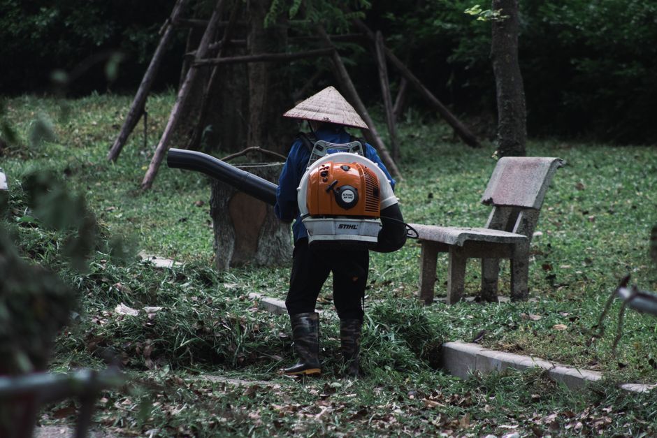 A gardener with a leaf blower maintains a park in Hanoi, Vietnam, surrounded by greenery.