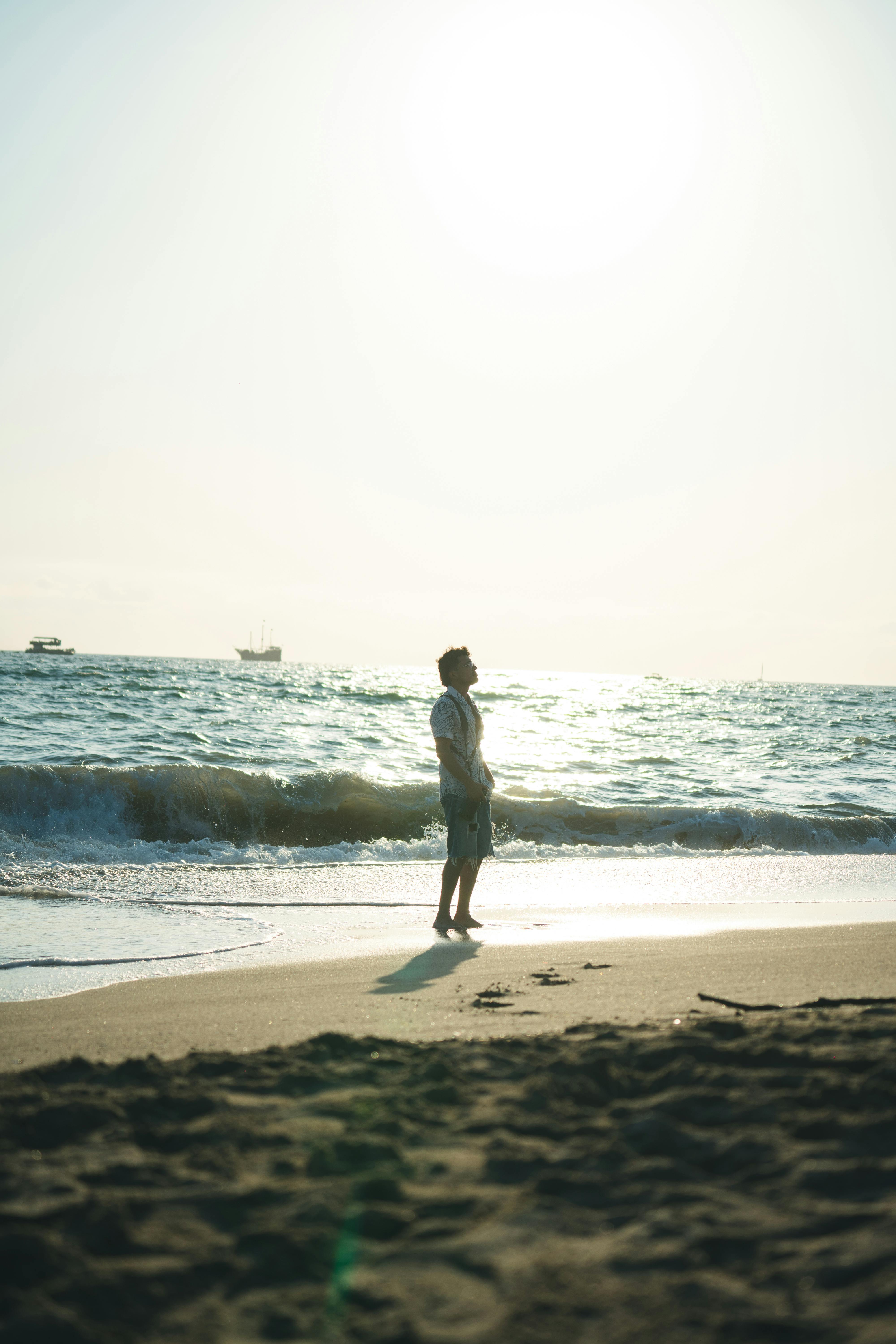 A man walks along a sunlit beach, enjoying the serene ocean view under a clear sky.