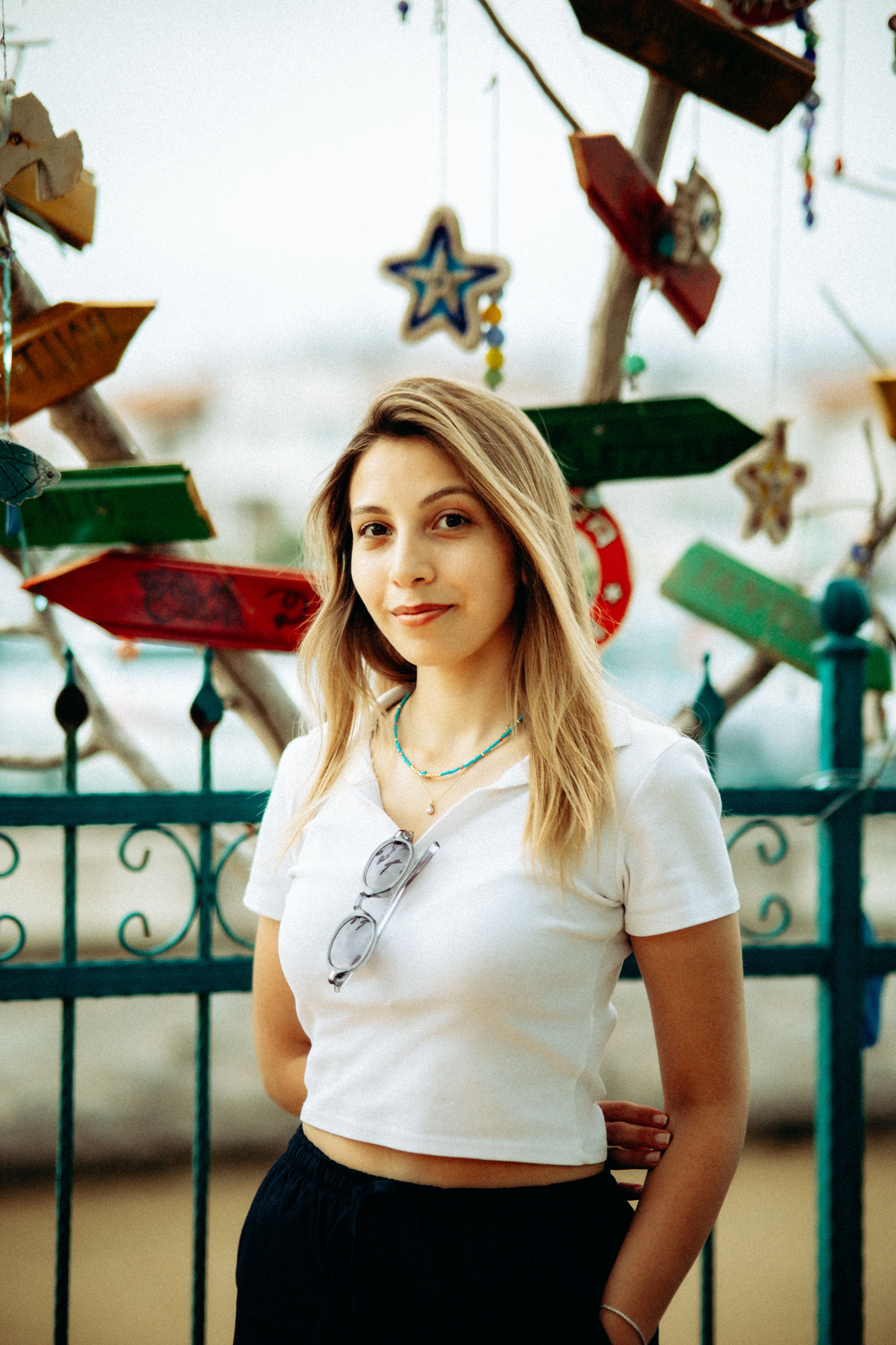 Young woman standing outdoors against decorative fence with hanging ornaments.