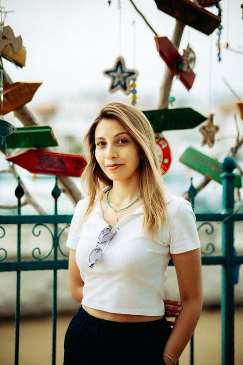 Free Young woman standing outdoors against decorative fence with hanging ornaments. Stock Photo