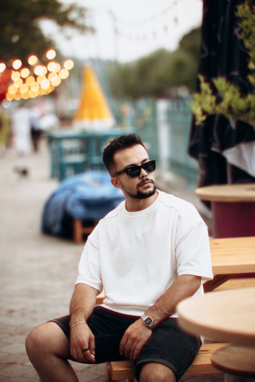 Free Stylish man in sunglasses and white t-shirt sitting at an outdoor café. Stock Photo
