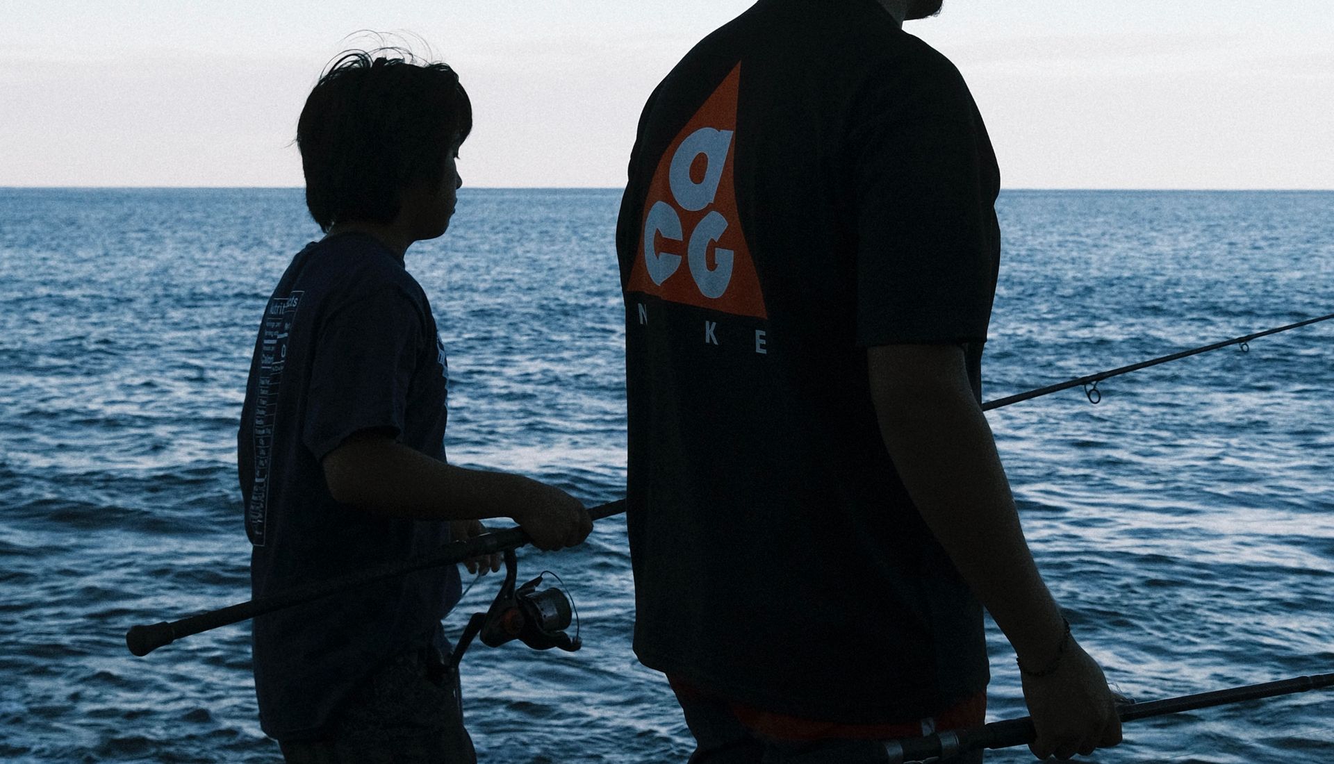 A father and son fishing from a rocky shore at dusk