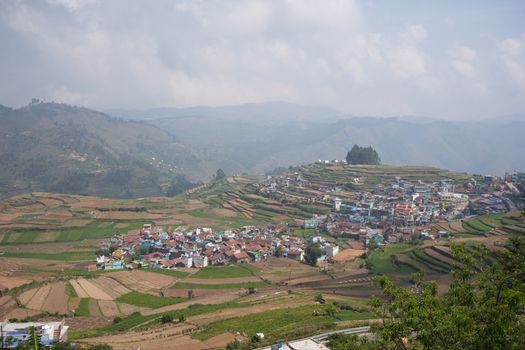 Aerial view of a village surrounded by lush terraced hills under a cloudy sky.