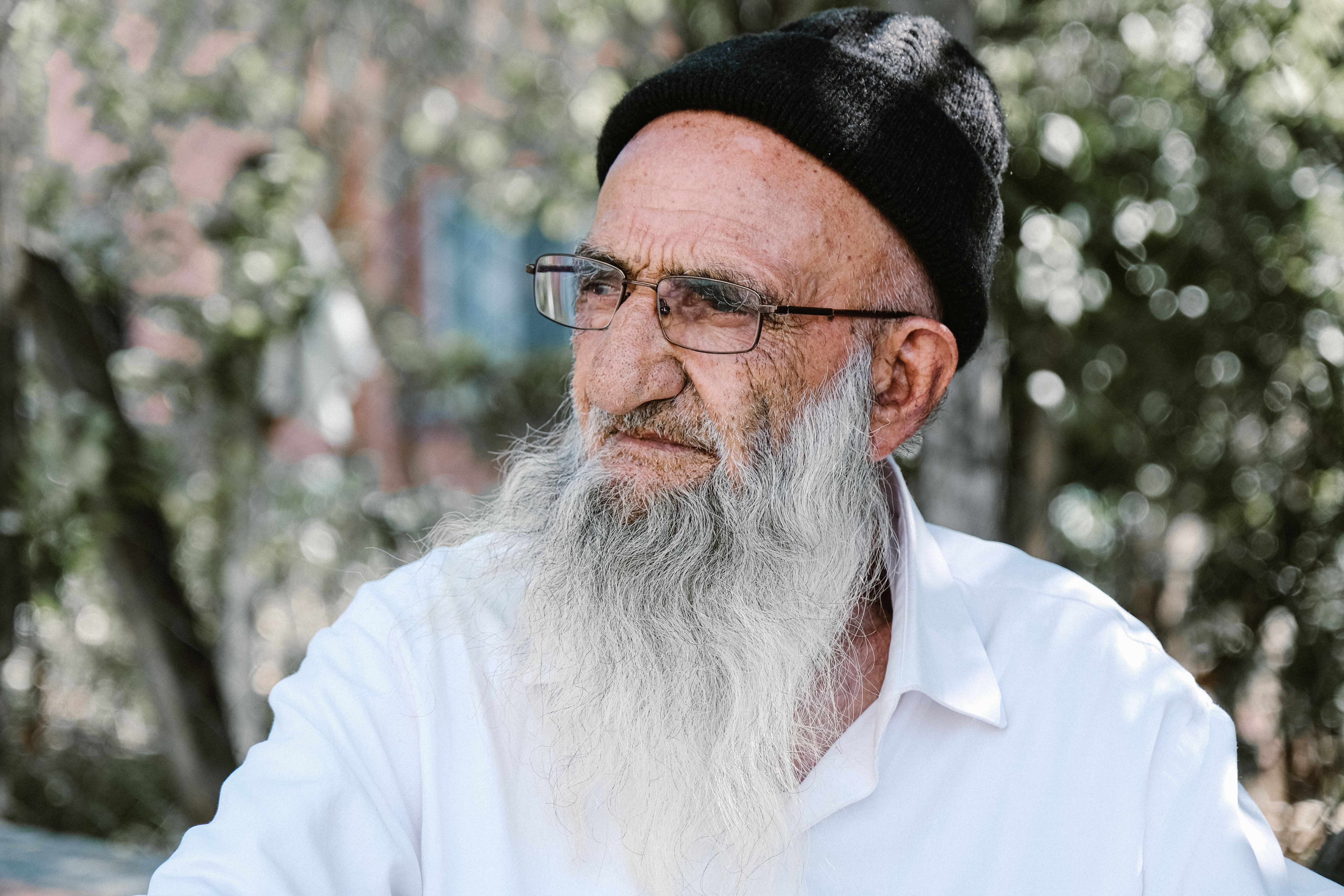 Elderly man with white beard outdoors in Istanbul, wearing a hat and glasses.