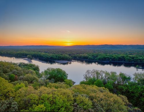 Free A breathtaking sunrise view over the Mississippi River with lush green trees and a golden horizon. Stock Photo