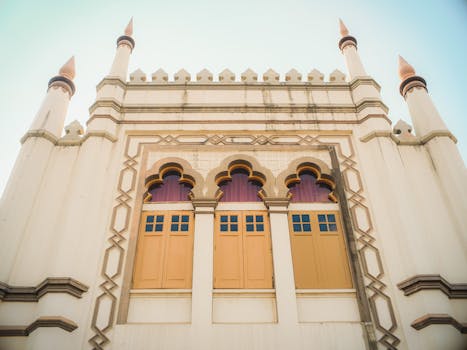 Low-angle view of a decorative building facade with three arched windows and ornate details.