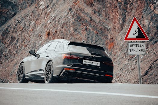 A modern luxury car parked on a scenic mountain road next to a landslide warning sign.