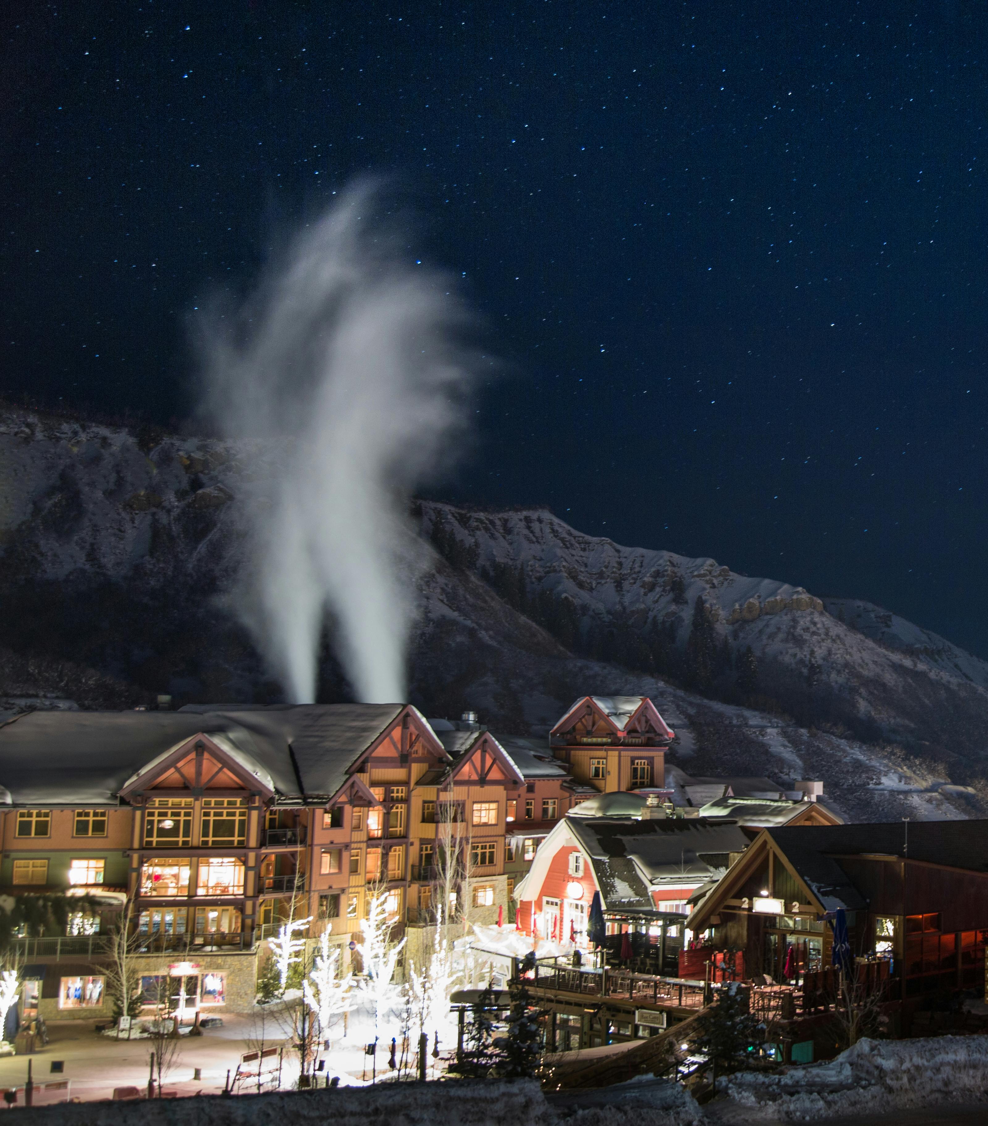 high angle shot of a beautiful town with wooden buildings and bright lights on the streets surrounded by scenic winter landscape