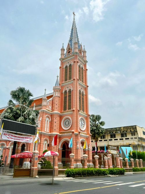 Free A vibrant pink Gothic Revival church amidst an urban Vietnam setting, with clear skies above. Stock Photo