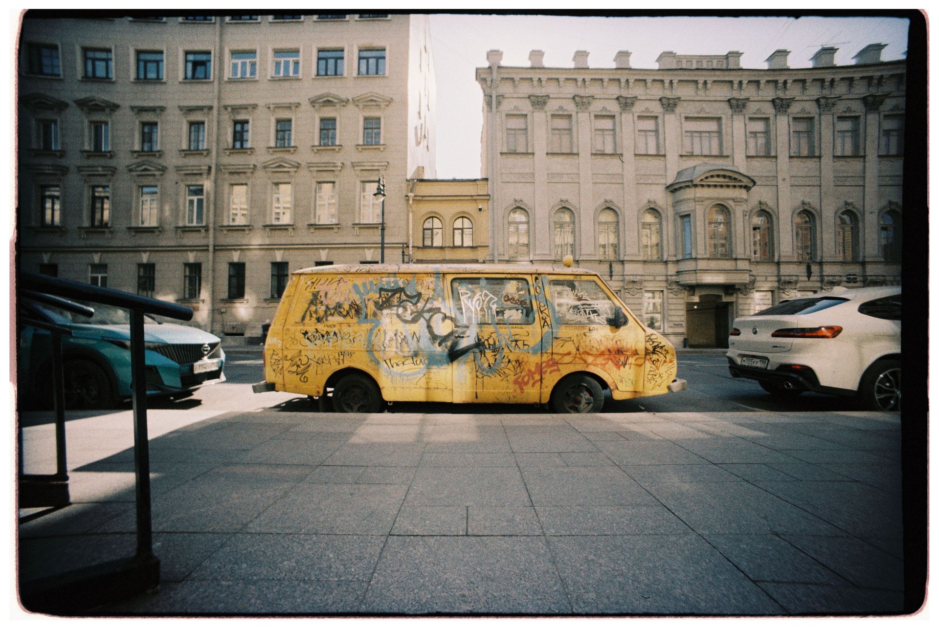 Yellow van with graffiti parked between buildings on a city street, showcasing urban art culture.