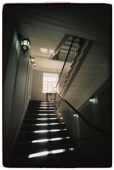 A vintage staircase illuminated by dramatic lighting through a window.