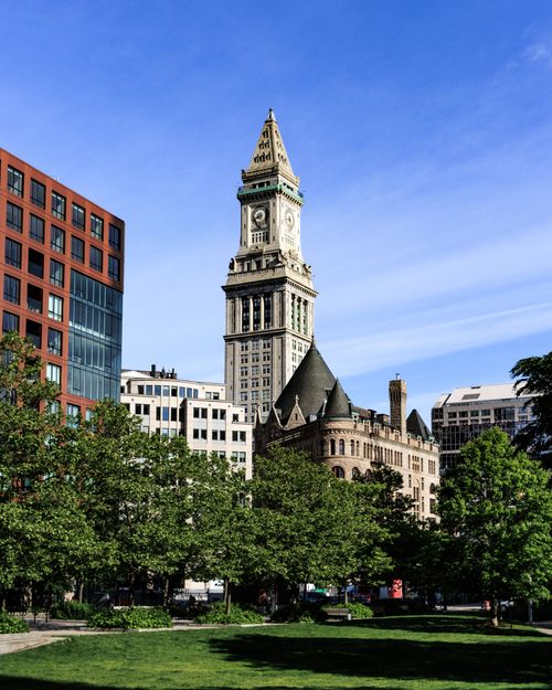 Free The historic Boston Custom House Tower with surrounding modern and historic architecture viewed from a green park. Stock Photo