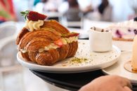 Mouthwatering croissant filled with cream and strawberries, served in a cozy cafe setting.