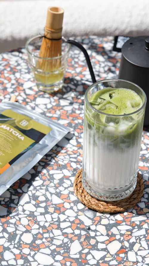 Free Iced matcha latte served on terrazzo table with bamboo whisk and tea set. Stock Photo