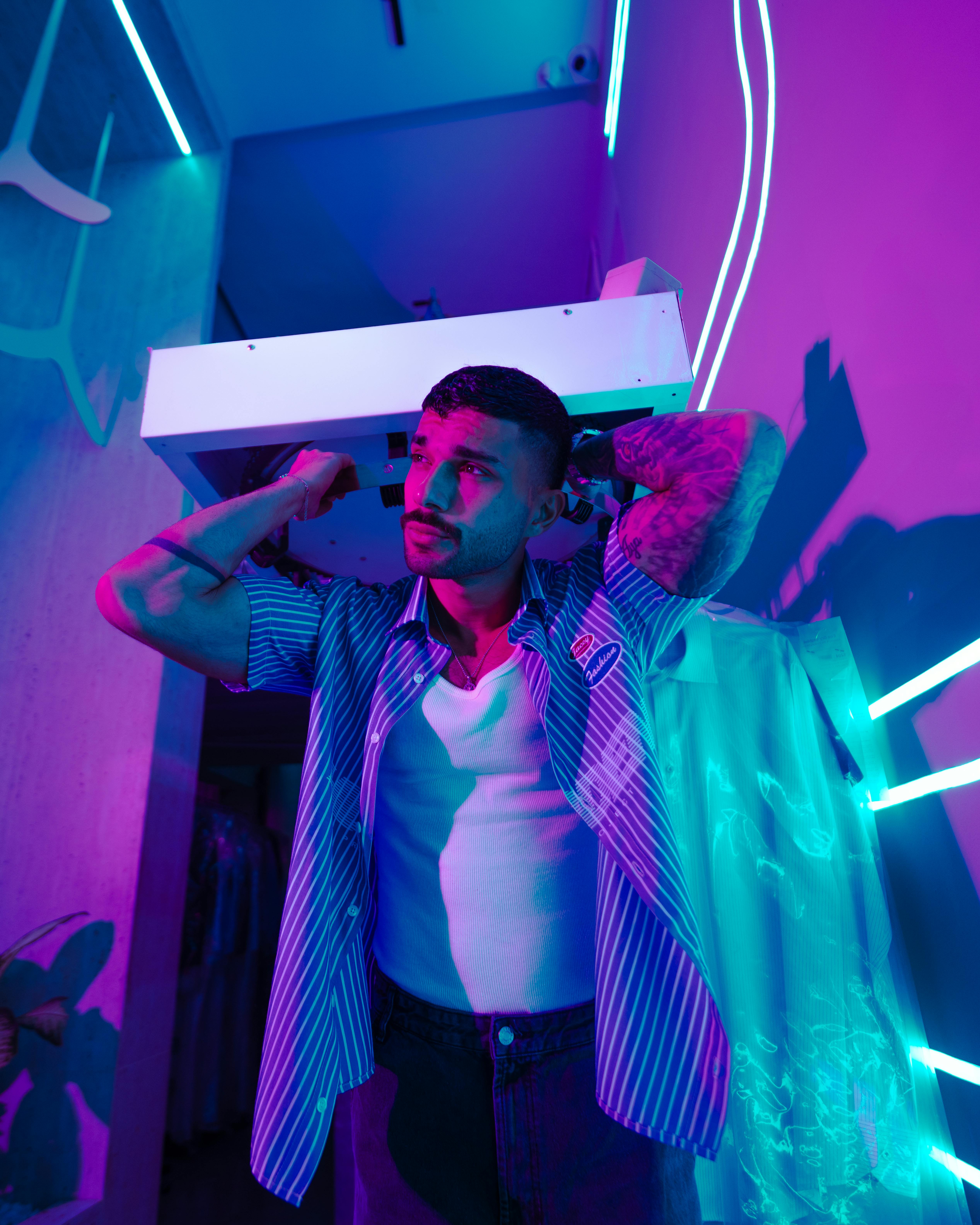 бесплатная Мужчина позирует под неоновым светом, создавая яркую и тревожную атмосферу в помещении. Стоковое фото