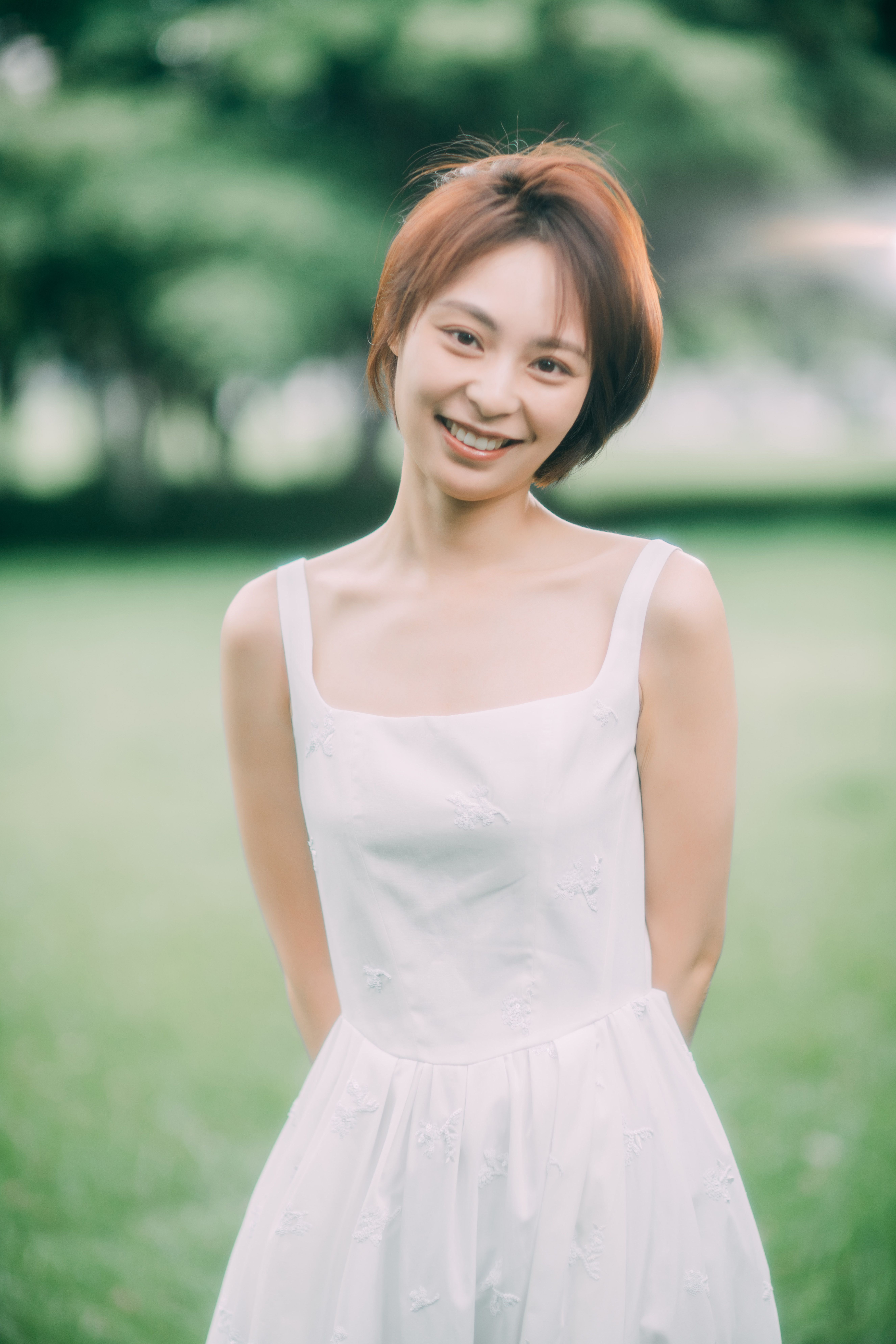 Smiling woman in white dress enjoying a sunny day in a lush park.