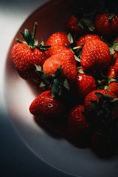 A close-up of fresh strawberries with dramatic natural lighting, highlighting texture and color.