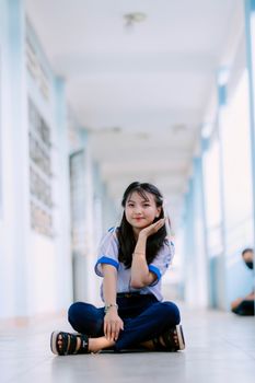 Casual portrait of a young woman sitting cross-legged in a bright school hallway.