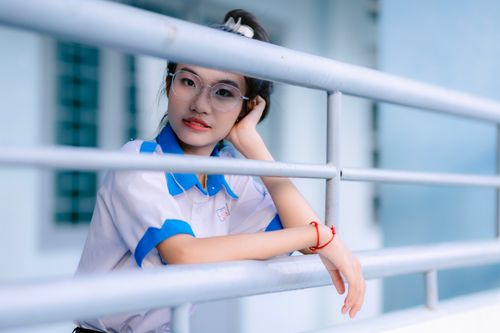 Free A teenage girl in school uniform leaning against a railing, gazing thoughtfully. Stock Photo